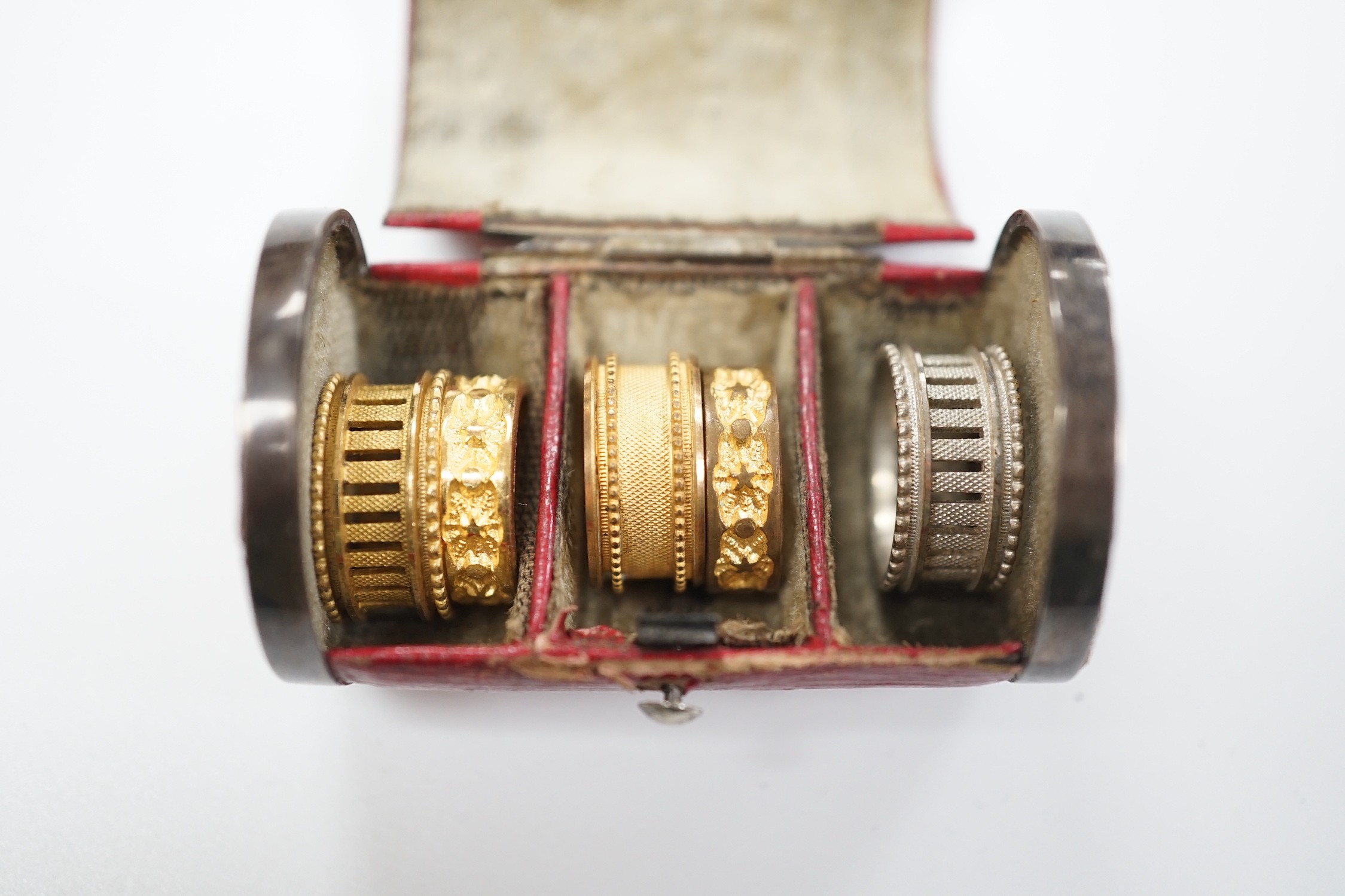 A rare Regency morocco leather mounted white metal cylindrical ring box containing five pinchbeck/base metal sample rings, box length 47mm.